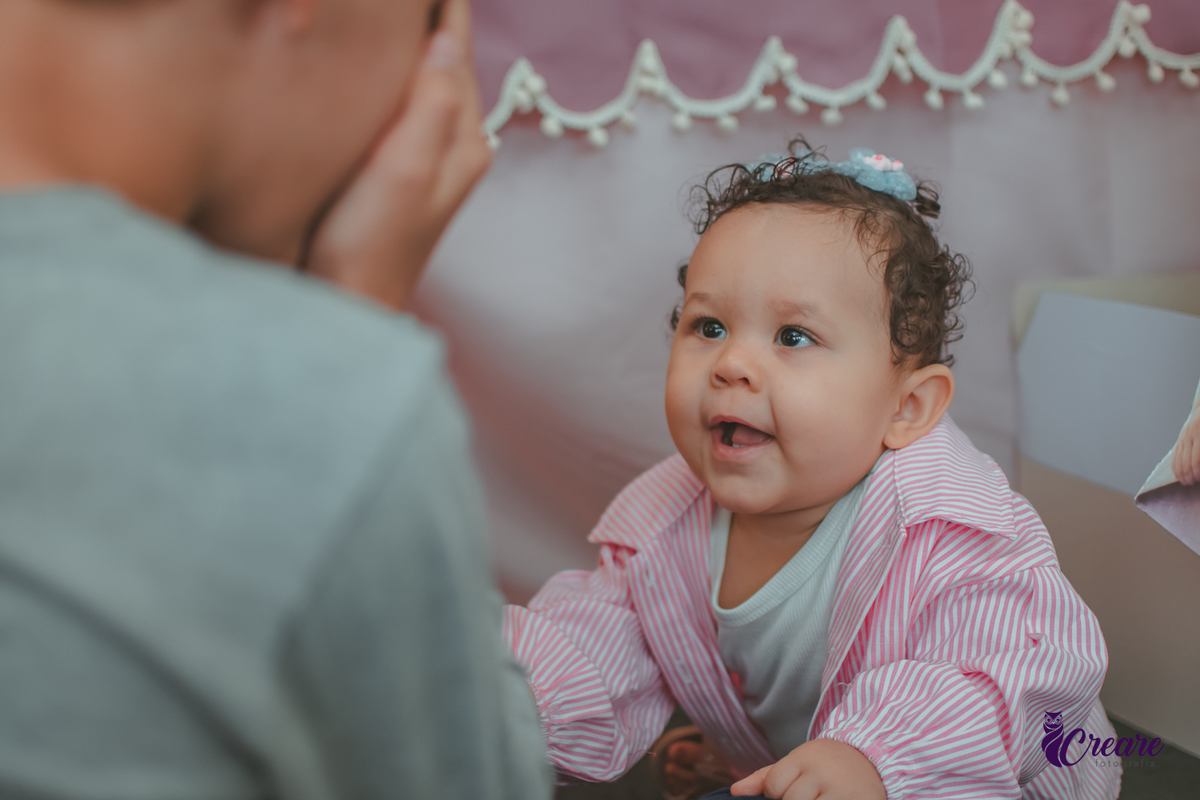 Uma bebê sorrindo e brincando durante festa de aniveersário em casa.