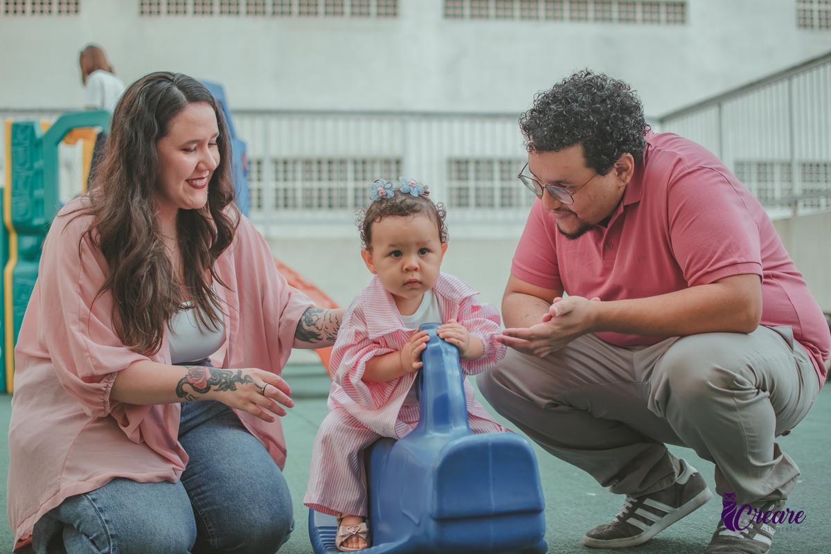 Uma bebê, brincando com seu pai e sua mãe em um parquinho de condomínio, durante festa de aniversário de 1 ano.