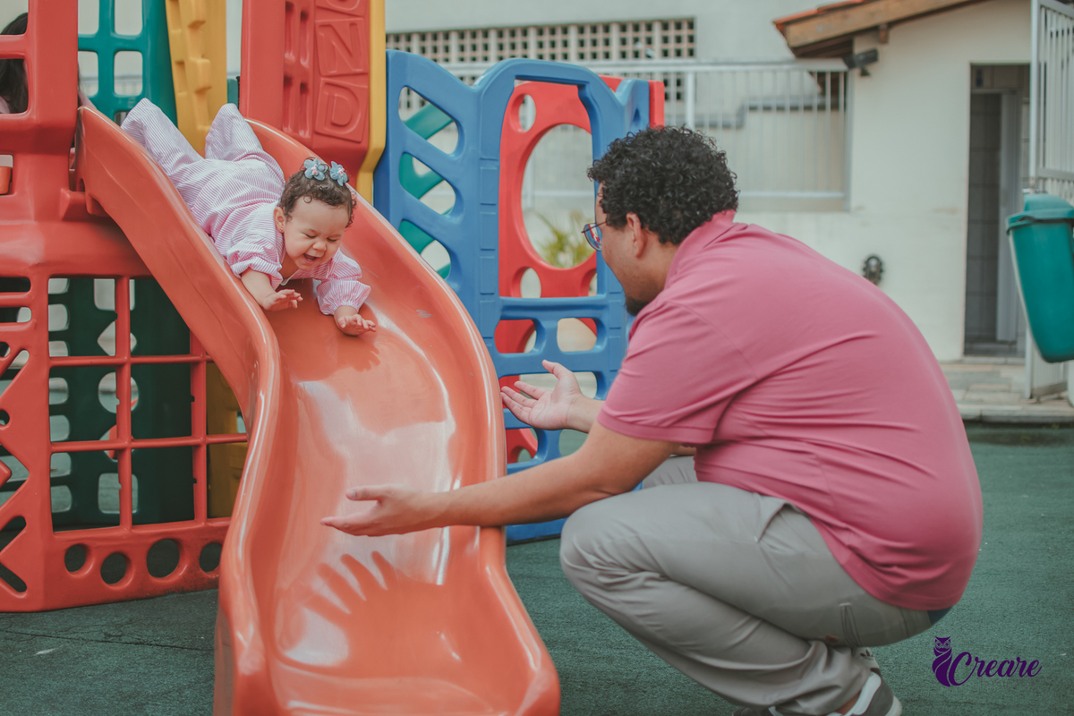 Uma bebê brincando com seu pai de descer no escorregador, durante sua festa de aniversário de 1 ano em casa.