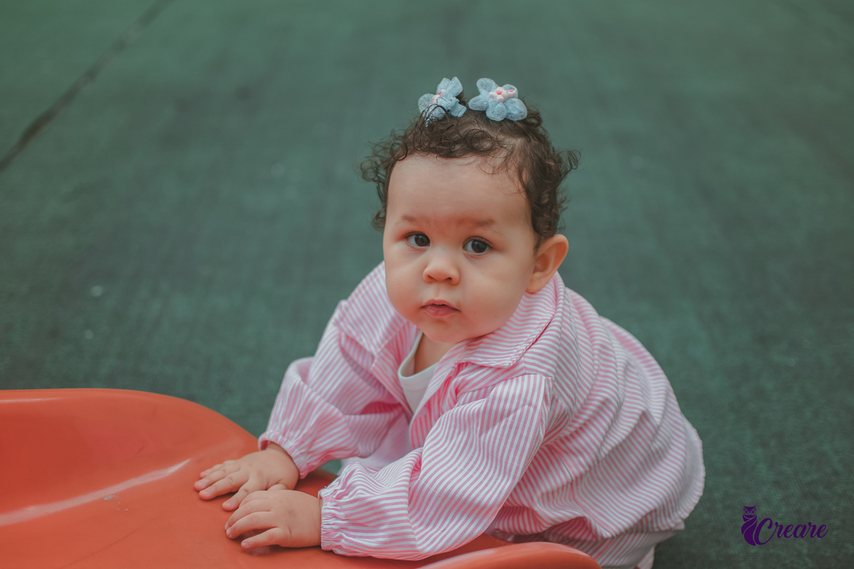 Uma bebê de 1 ano, brincando no parquinho do condomínio, durante sua festa de aniversário em casa.