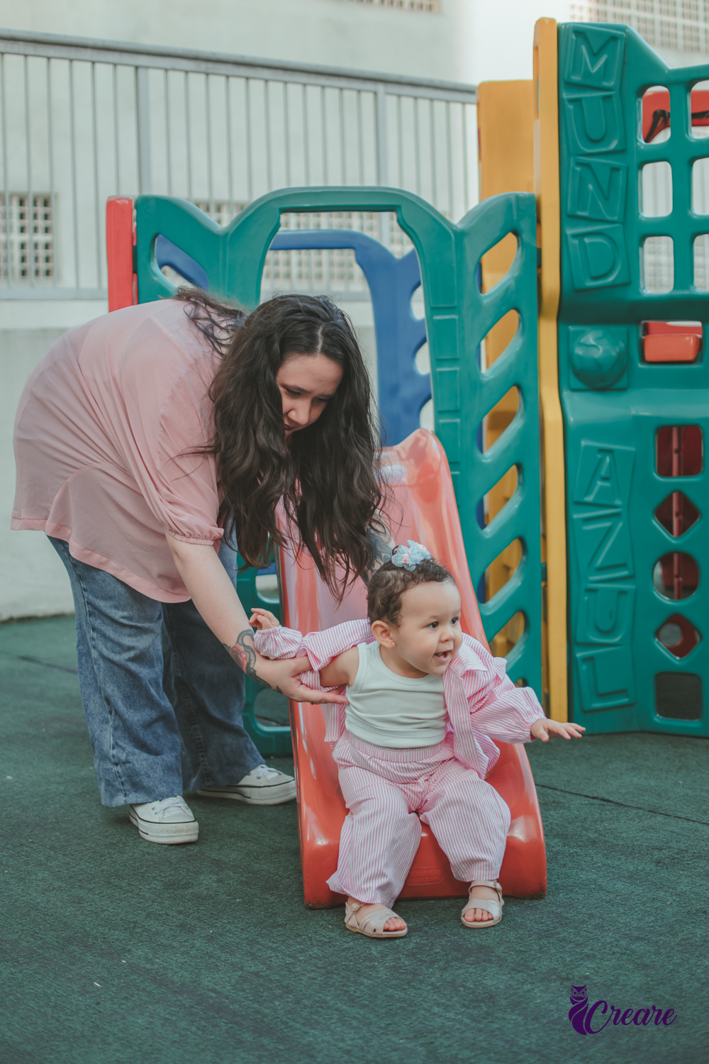 Uma bebê brincando no escorregador com sua mãe, durante festa de aniversário de 1 ano em casa.
