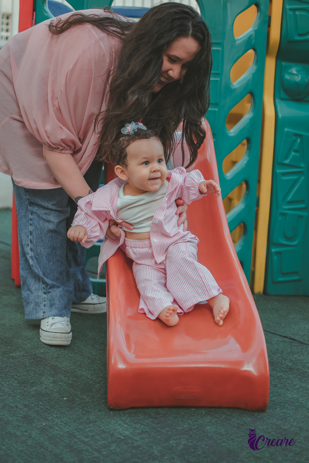 Uma bebê brincando no escorregador com sua mãe, durante festa de aniversário de 1 ano em casa.