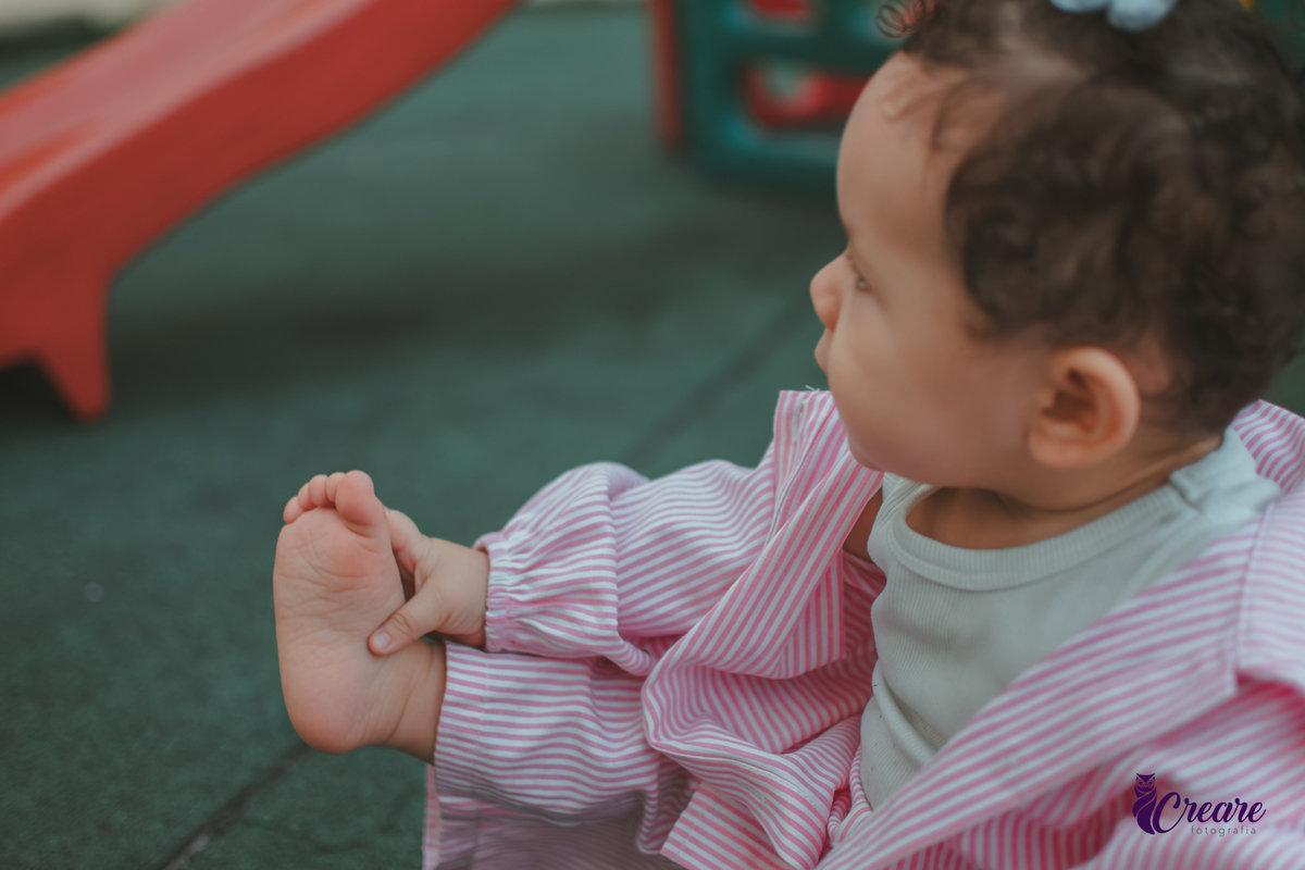 Uma bebê brincando com os pés, durante festa de aniversário de 1 ano em casa.
