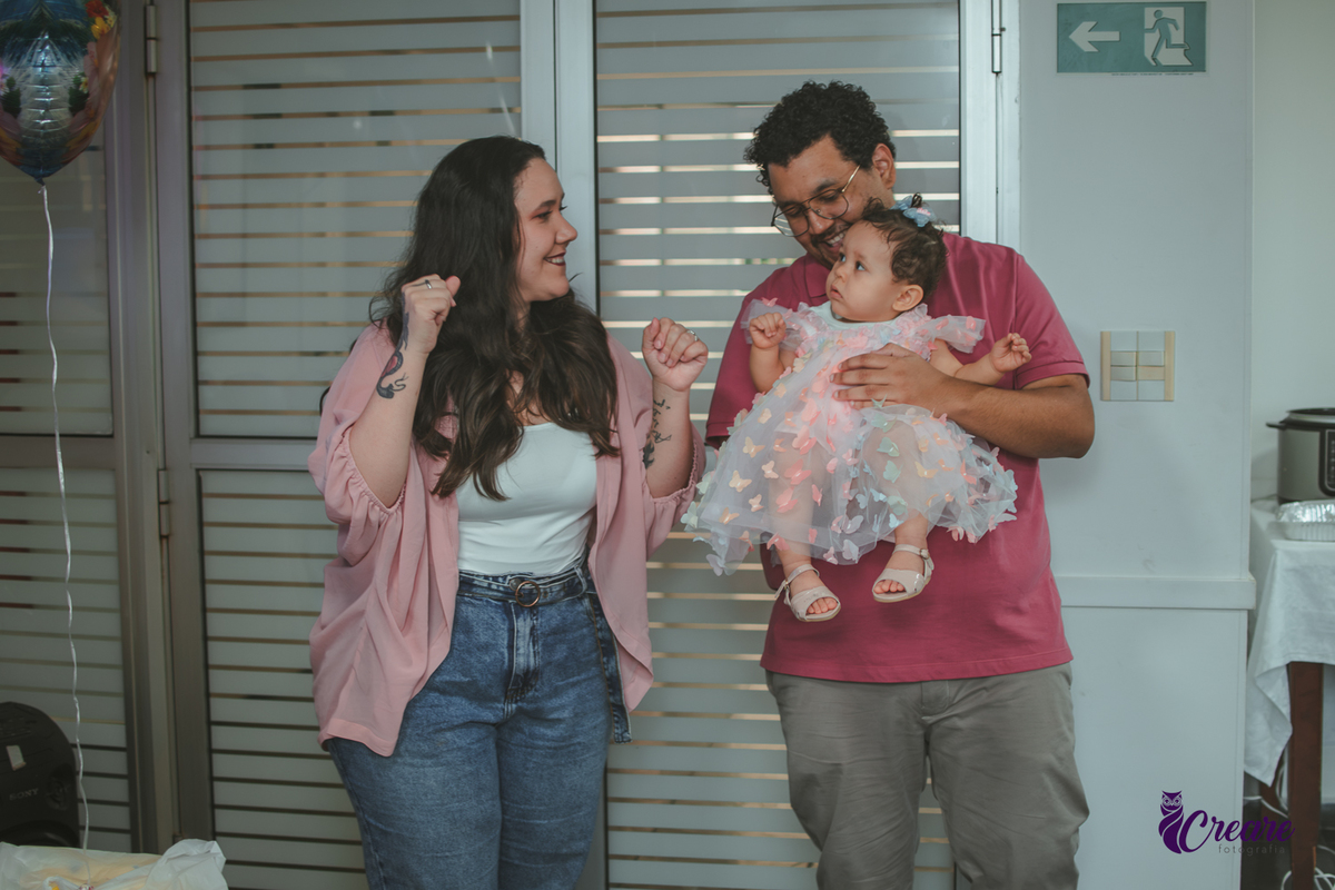 Um casal, dançando com uma bebê no colo, durante festa de aniversário infantil.