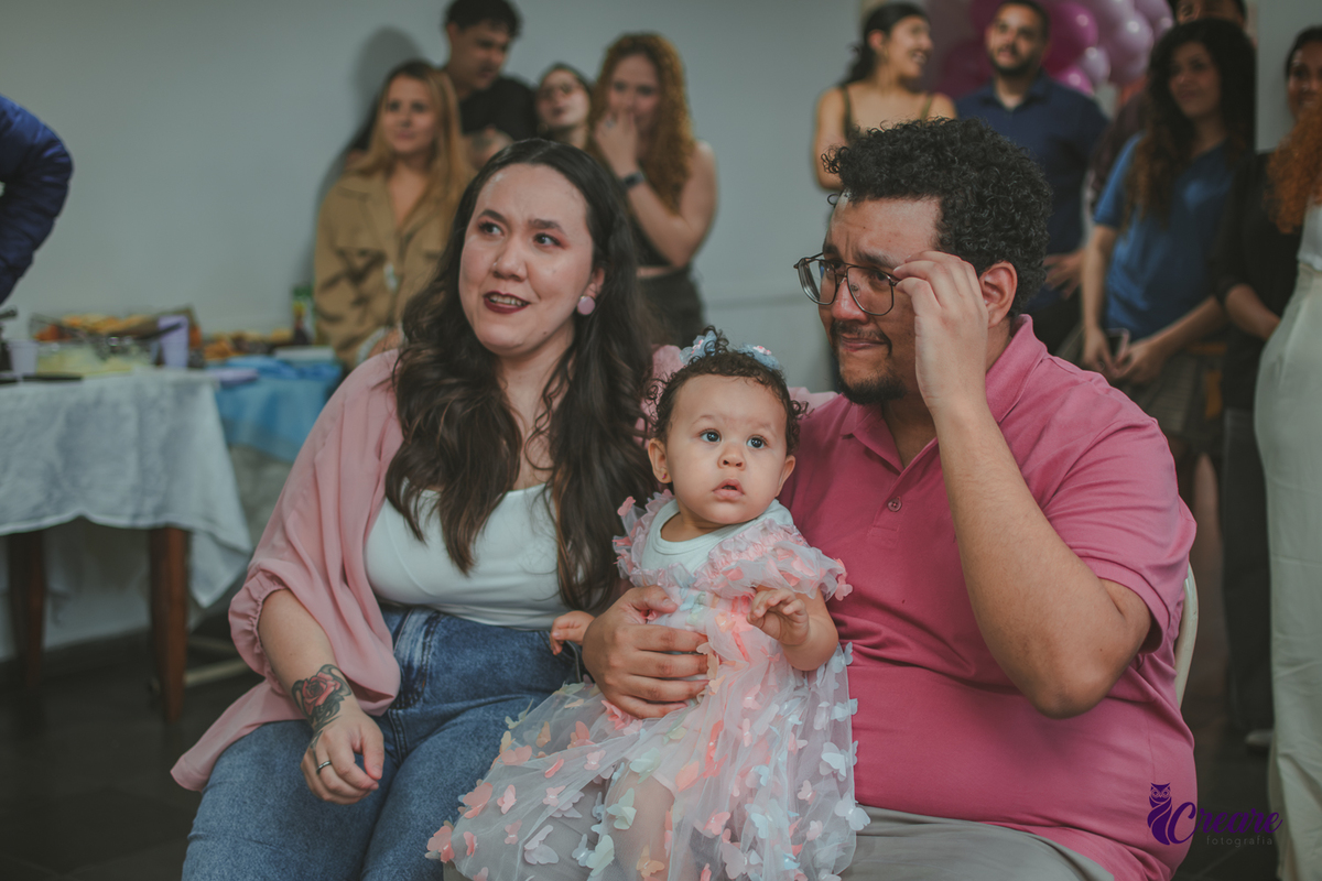 Um casal emocionado assistindo a restrospectiva, durante festa de aniversário de 1 ano em casa.