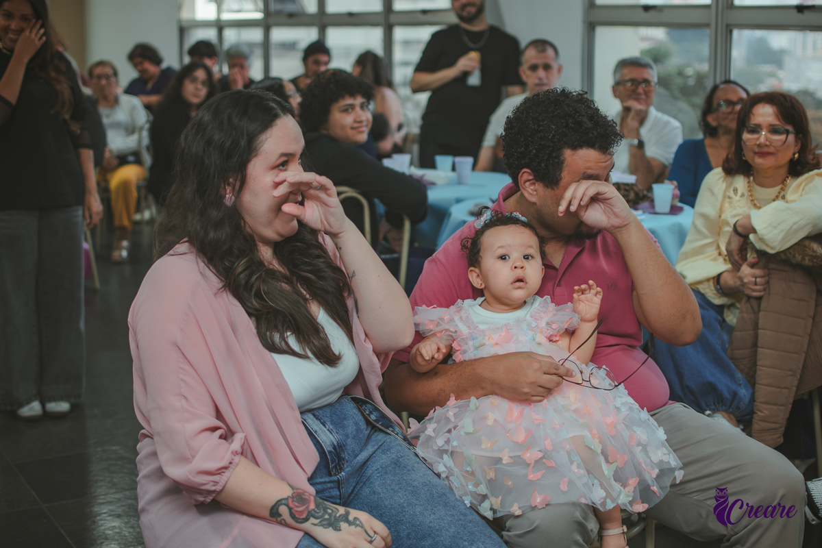 Um casal emocionado assistindo a restrospectiva, durante festa de aniversário de 1 ano em casa.