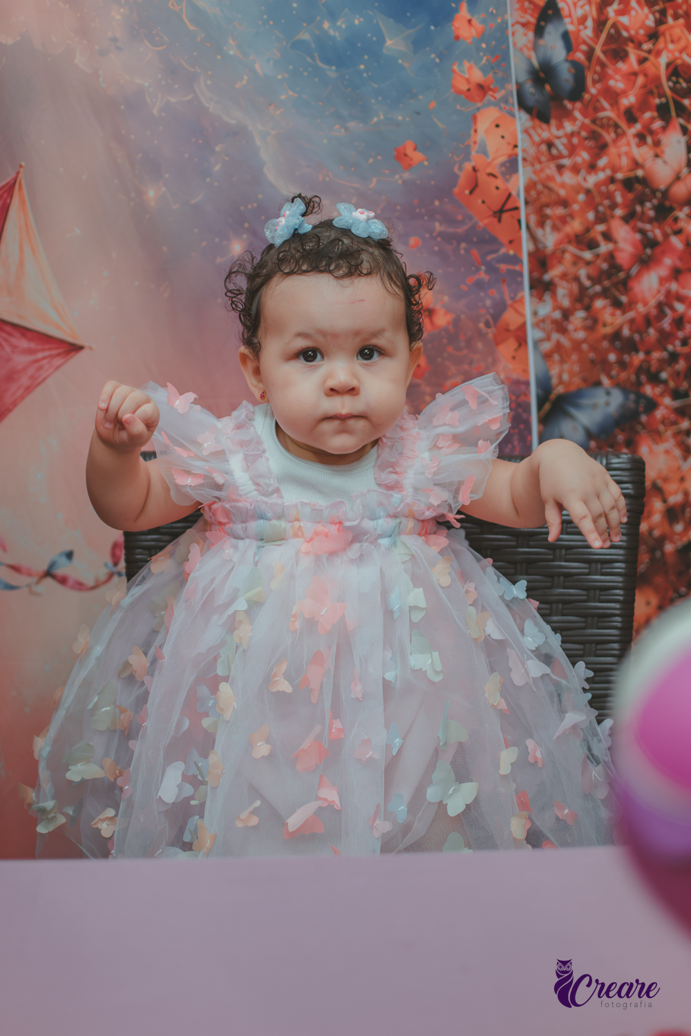 Uma bebê usando vestido de borboletas, durante sua festa de aniversário de 1 ano.