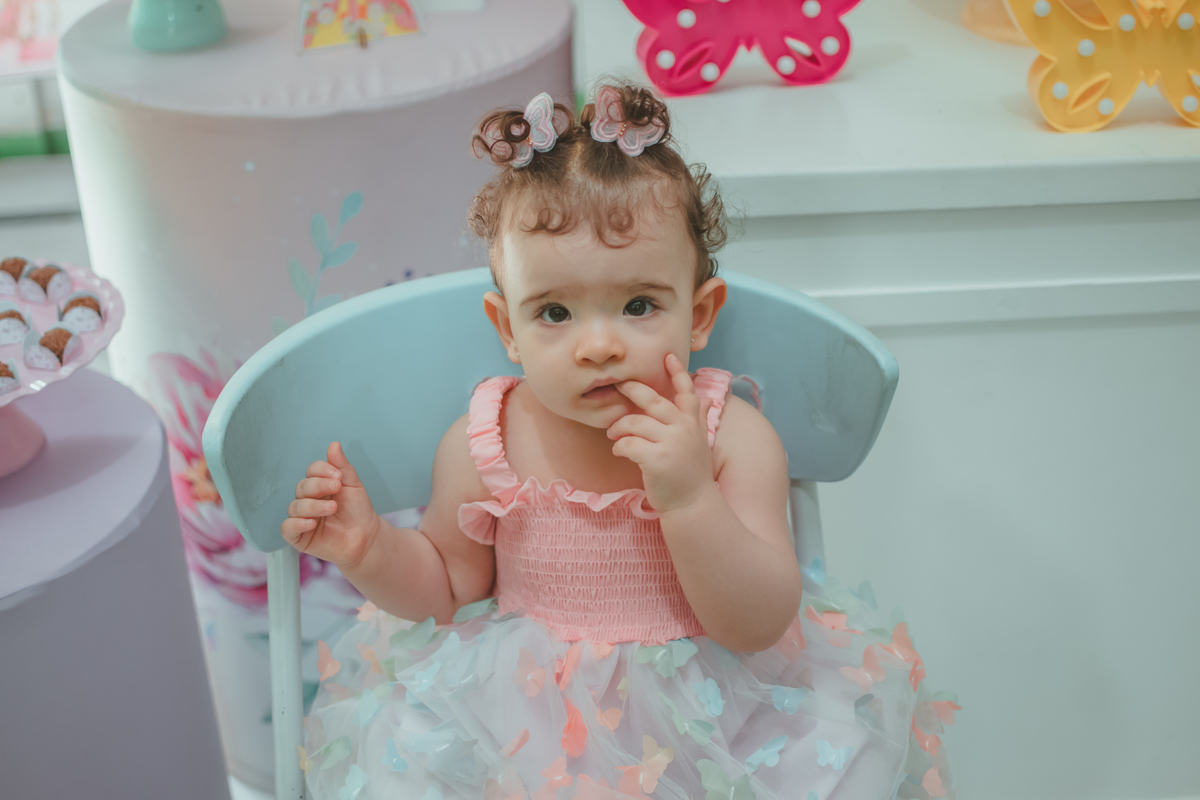 Uma bebê sentanda em frente a decoração da sua festa de aniversário de 1 ano com tema borboletas.