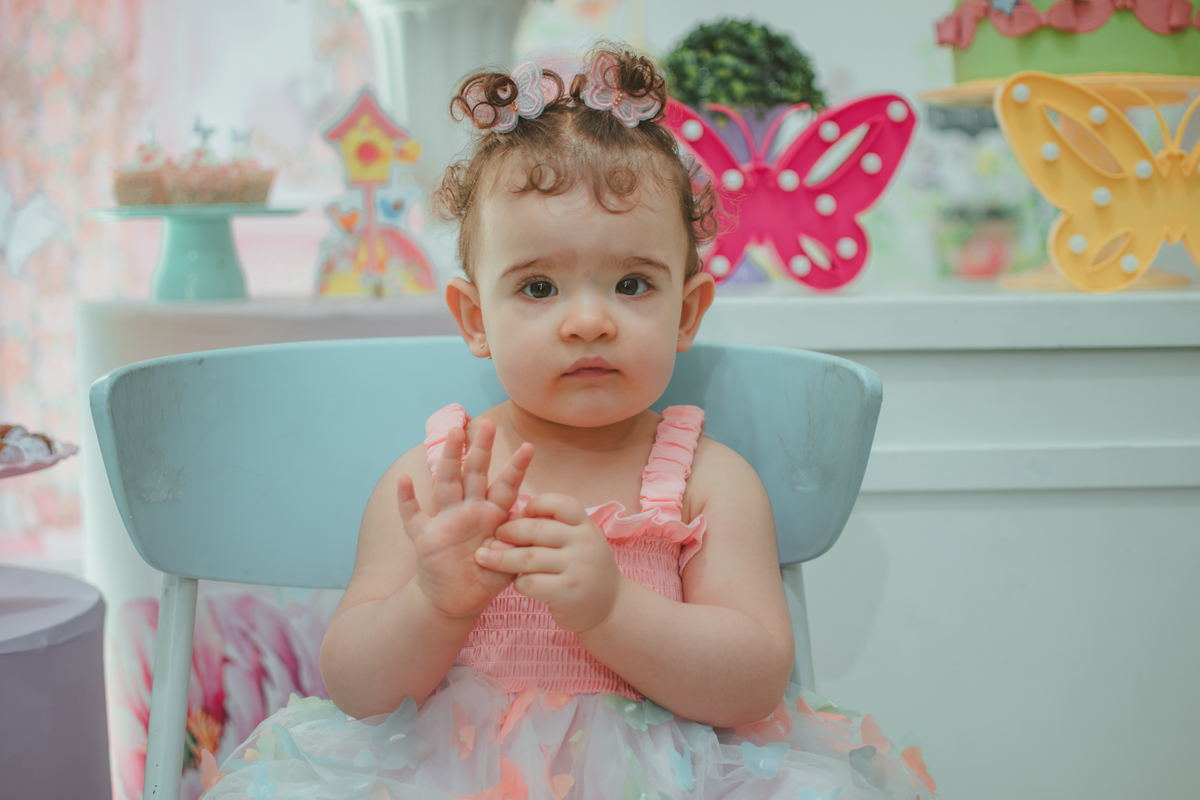 Uma bebê sentanda em frente a decoração da sua festa de aniversário de 1 ano com tema borboletas.