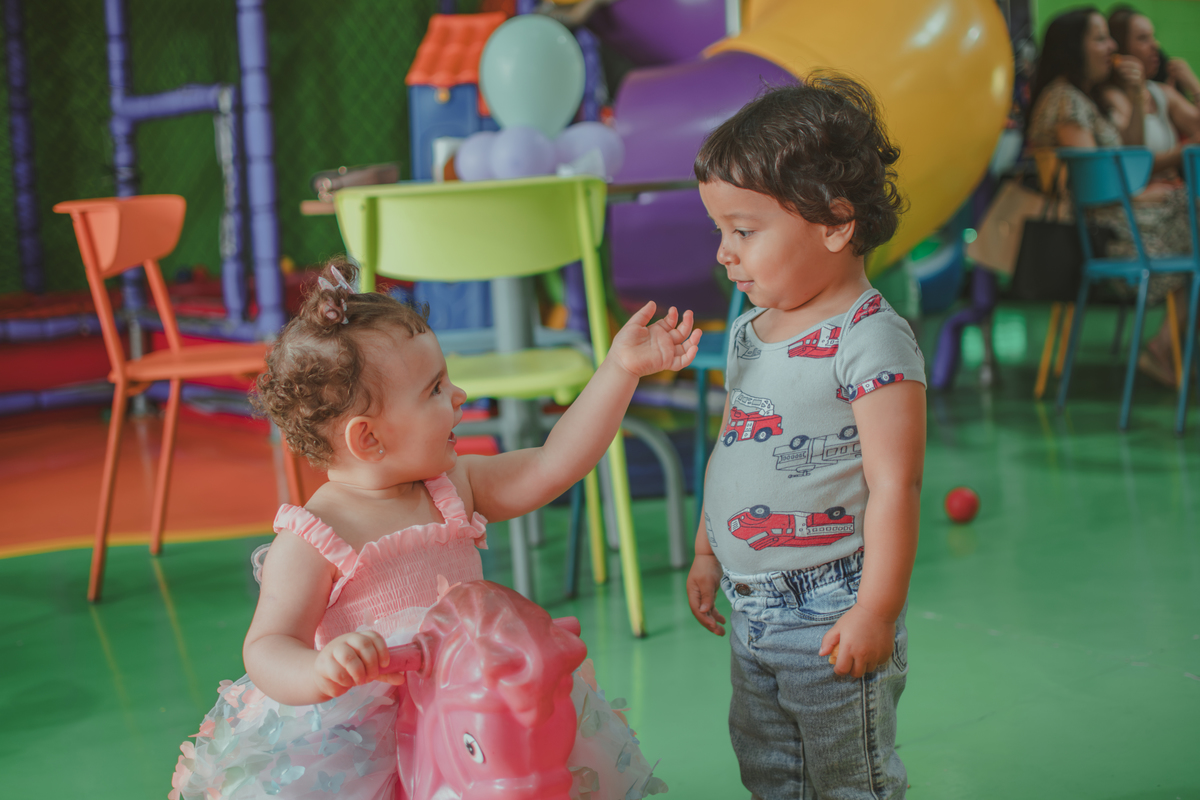Uma bebê em um brinquedo em formato de cavalinho rosa, durante festa de aniversário infantil.