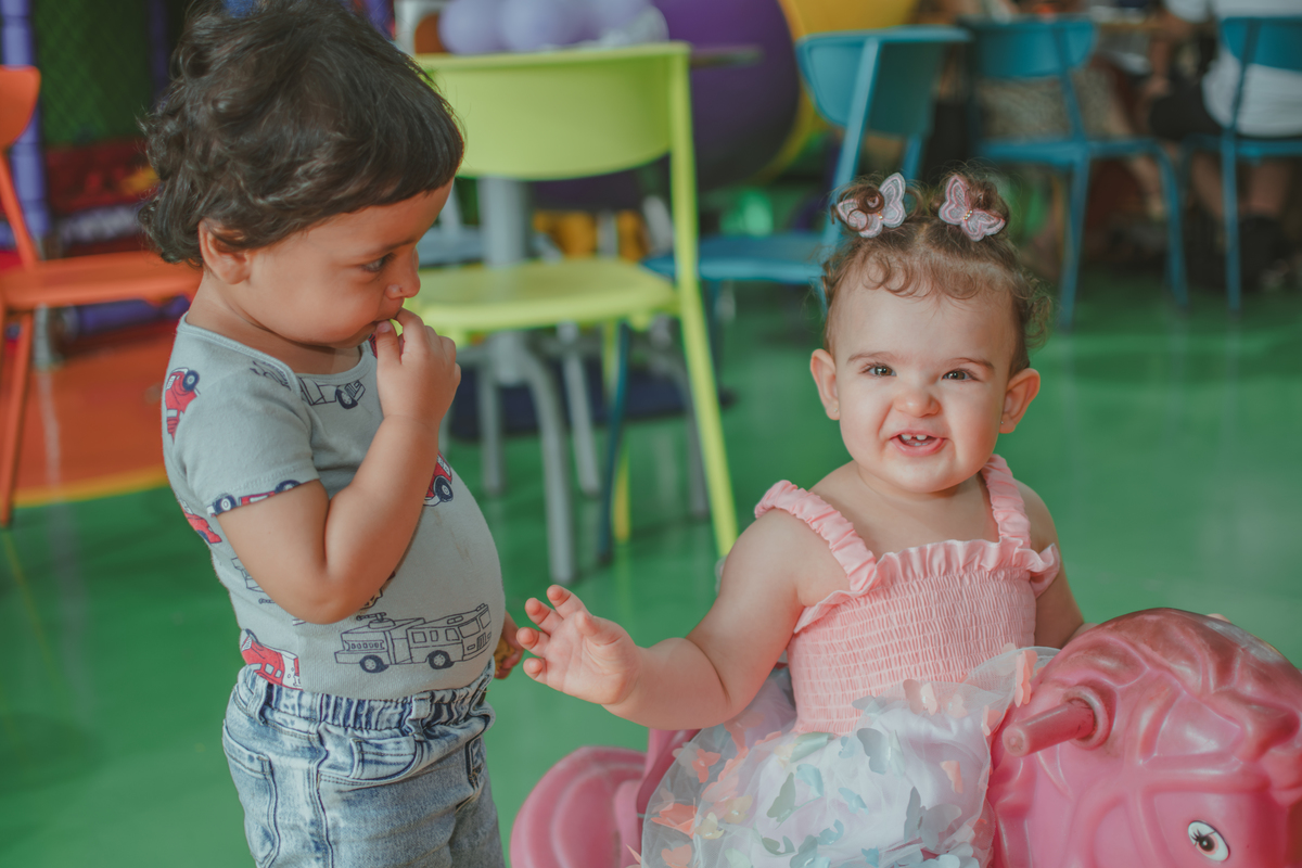 Uma bebê em um brinquedo em formato de cavalinho rosa, durante festa de aniversário infantil.