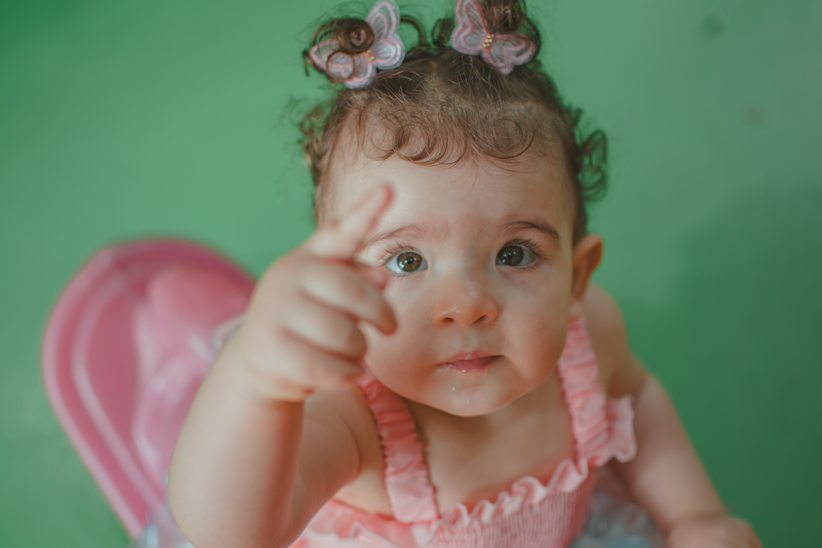 Uma bebê em um brinquedo em formato de cavalinho rosa, durante festa de aniversário infantil.