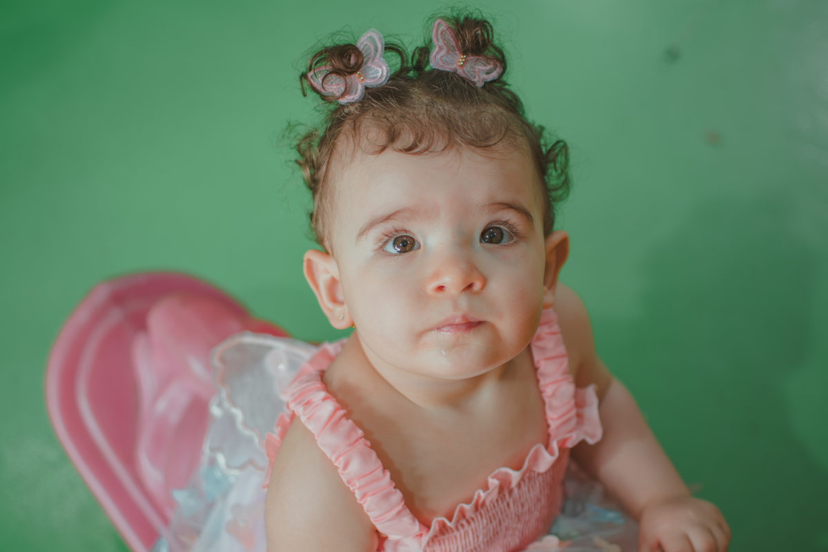 Uma bebê em um brinquedo em formato de cavalinho rosa, durante festa de aniversário infantil.