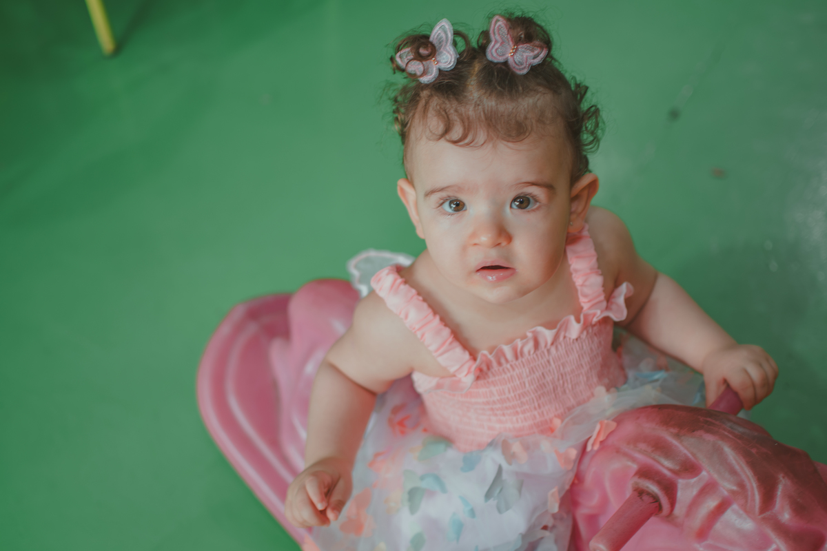 Uma bebê em um brinquedo em formato de cavalinho rosa, durante festa de aniversário infantil.