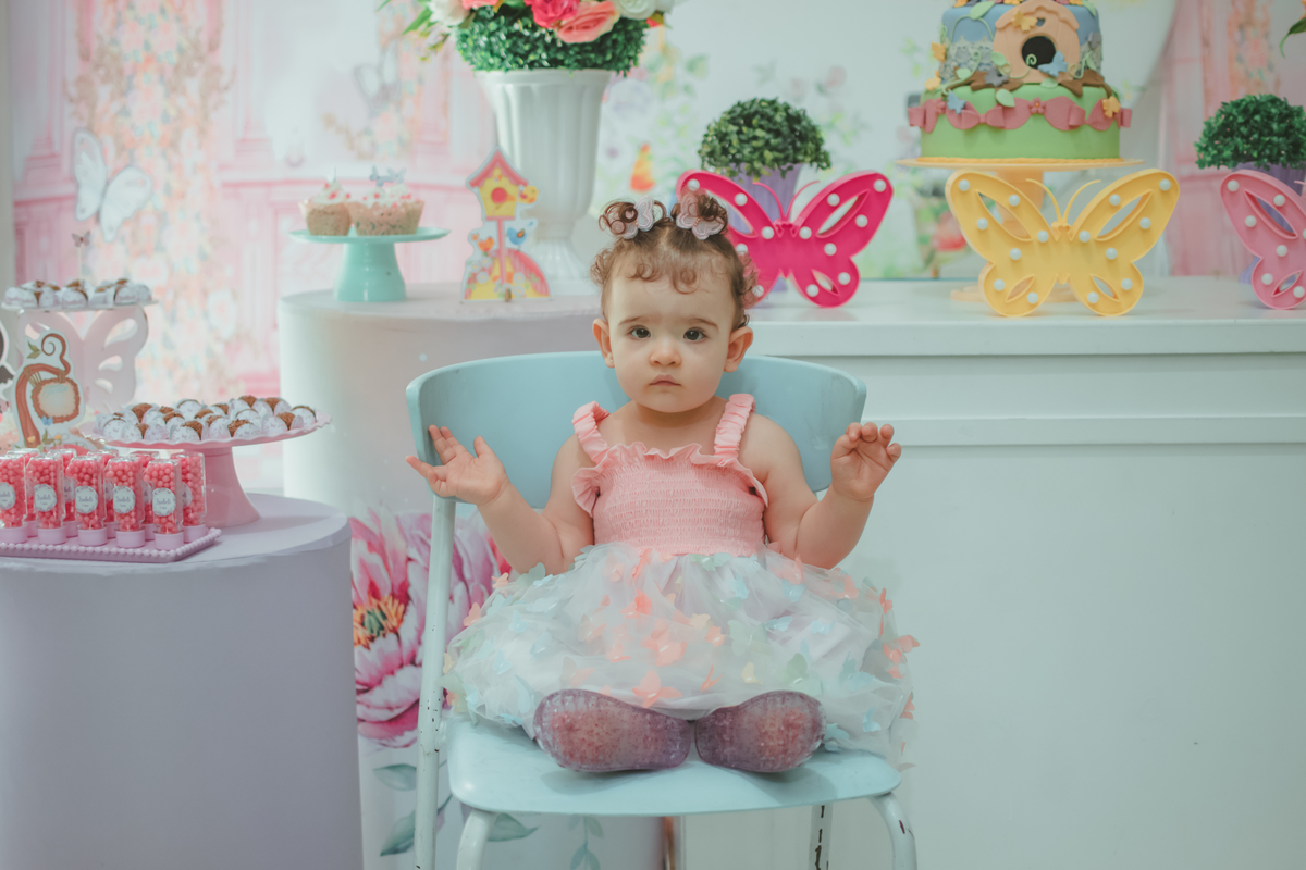Uma bebê sentanda em frente a decoração da sua festa de aniversário de 1 ano com tema borboletas.