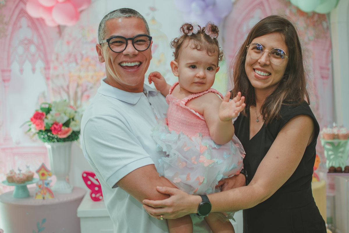 Uma casal com uma bebê no colo, durante aniversário de 1 ano.