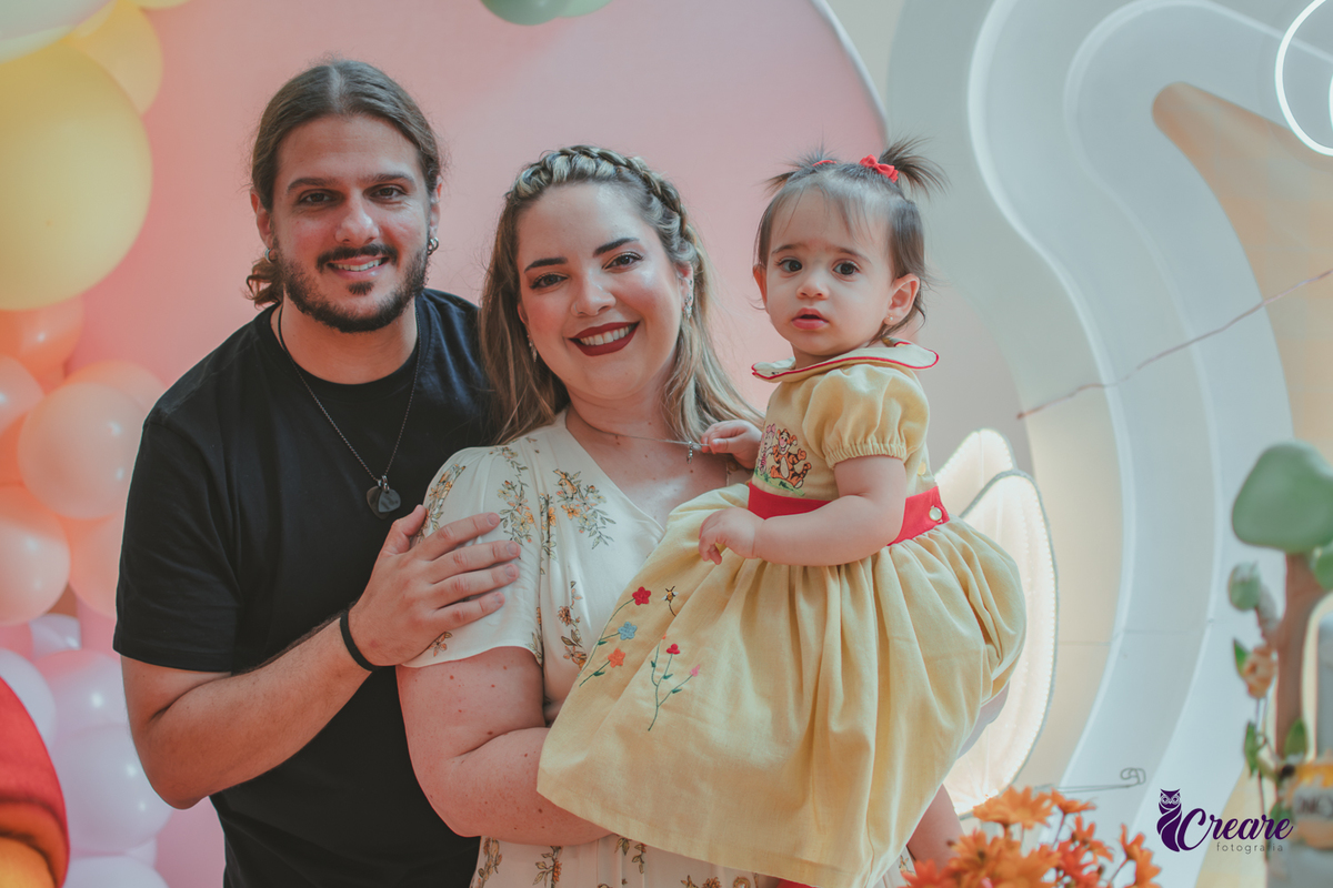 Uma familia com uma bebê de 1 ano em frente a decoração da festa de aniversário feita em casa.