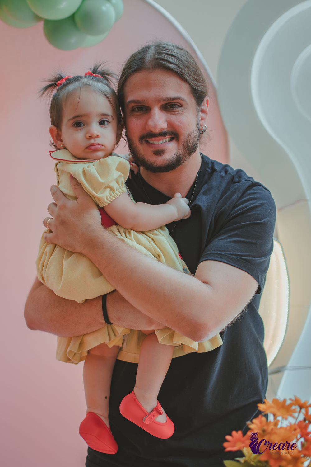 Um Homem com uma bebê de 1 ano em frente a decoração da festa de aniversário feita em casa.