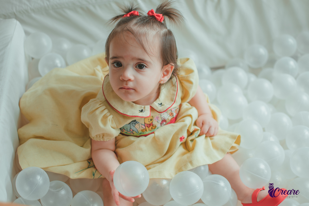 Uma bebê brincando na piscina de bolinhas brancas, durante sua festa de aniversário de 1 ano.