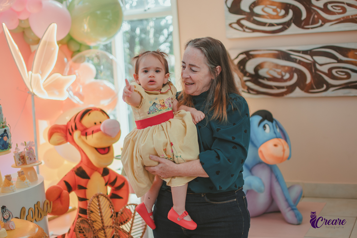 Uma mulher com uma bebê no colo, durante sua festa de aniversário de 1 ano em casa.
