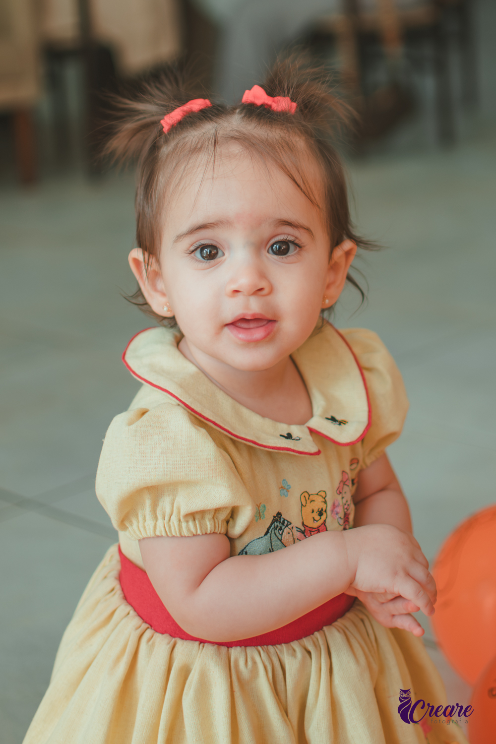 Uma bebê brincando entre balões amarelos e laranjaas, durante sua festa de aniversário de 1 ano em casa.
