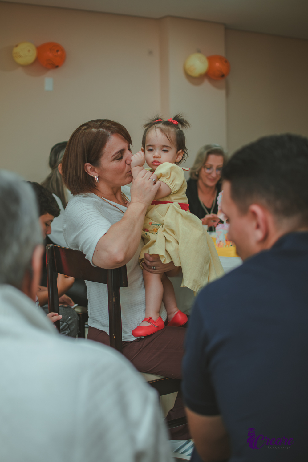Um mulher beijando a mão de uma bebê durante sua festa de aniversário de 1 ano em casa.