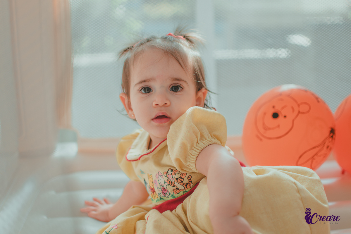 Uma bebê brincando no brinquedo inflável, Cercada por balões laranjas, durante sua festa de aniversário de 1 ano.
