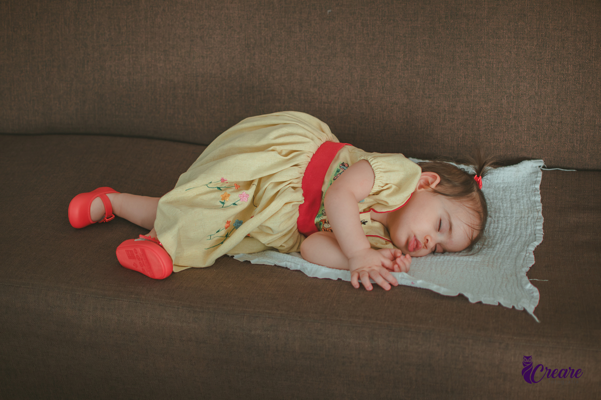 Uma bebê dormindo no sofá marrom, durante sua festa de aniversário em casa.