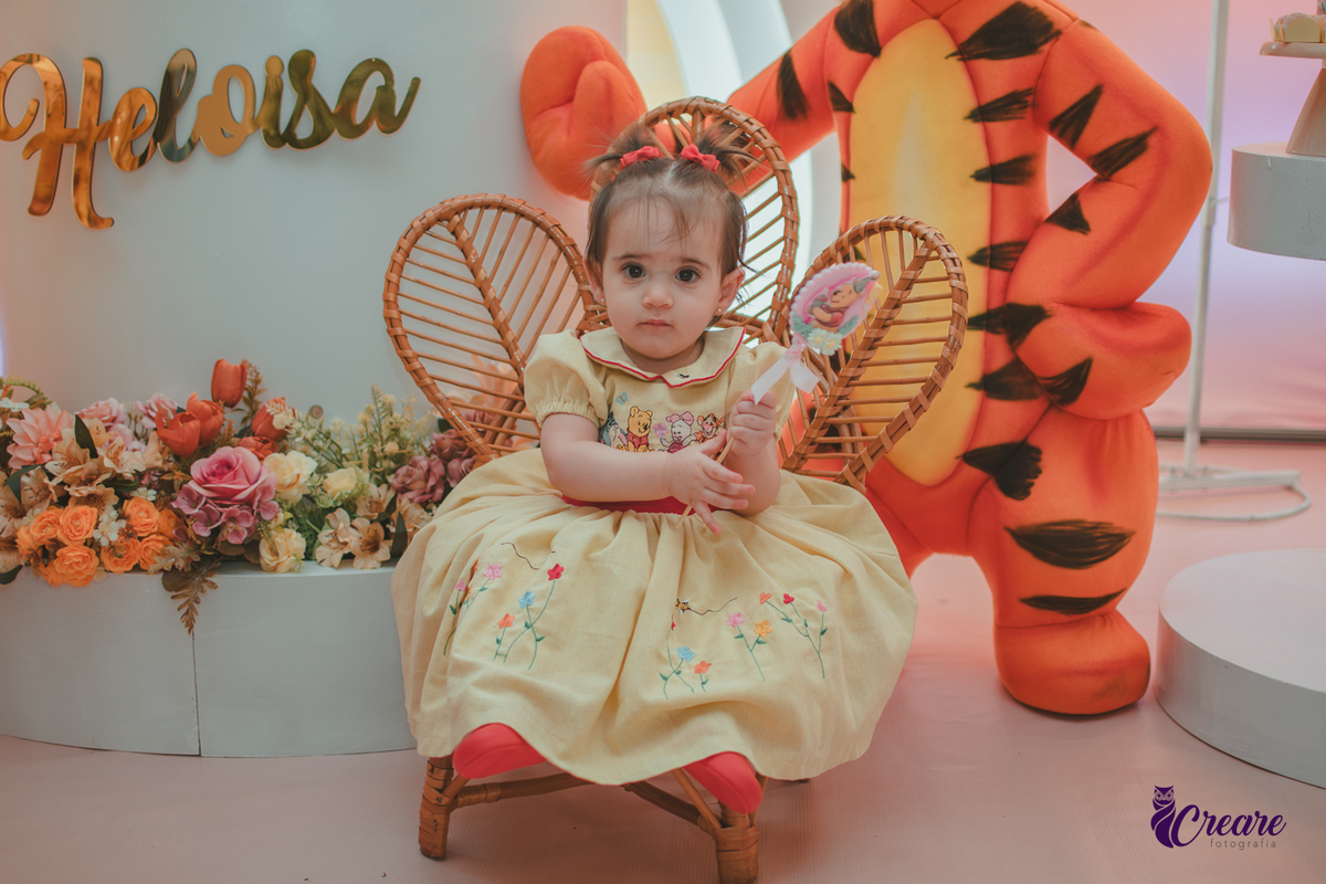 Uma bebê sentanda em frente a decoração da sua festa de aniversário e seguntando uma pirulito de chocolate.