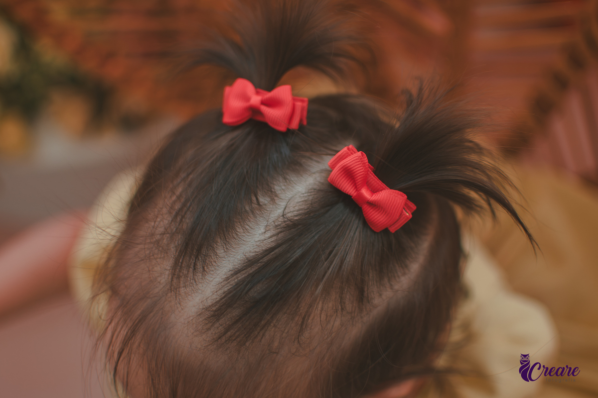 Detalhes dos lacinhos vermelhos do cabelo de uma bebê de 1 ano.