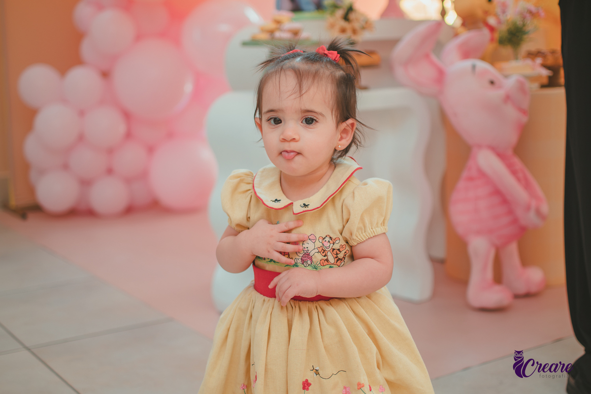 Uma bebê de 1 ano, andando pelo salão da sua festa de aniversário feita em casa.