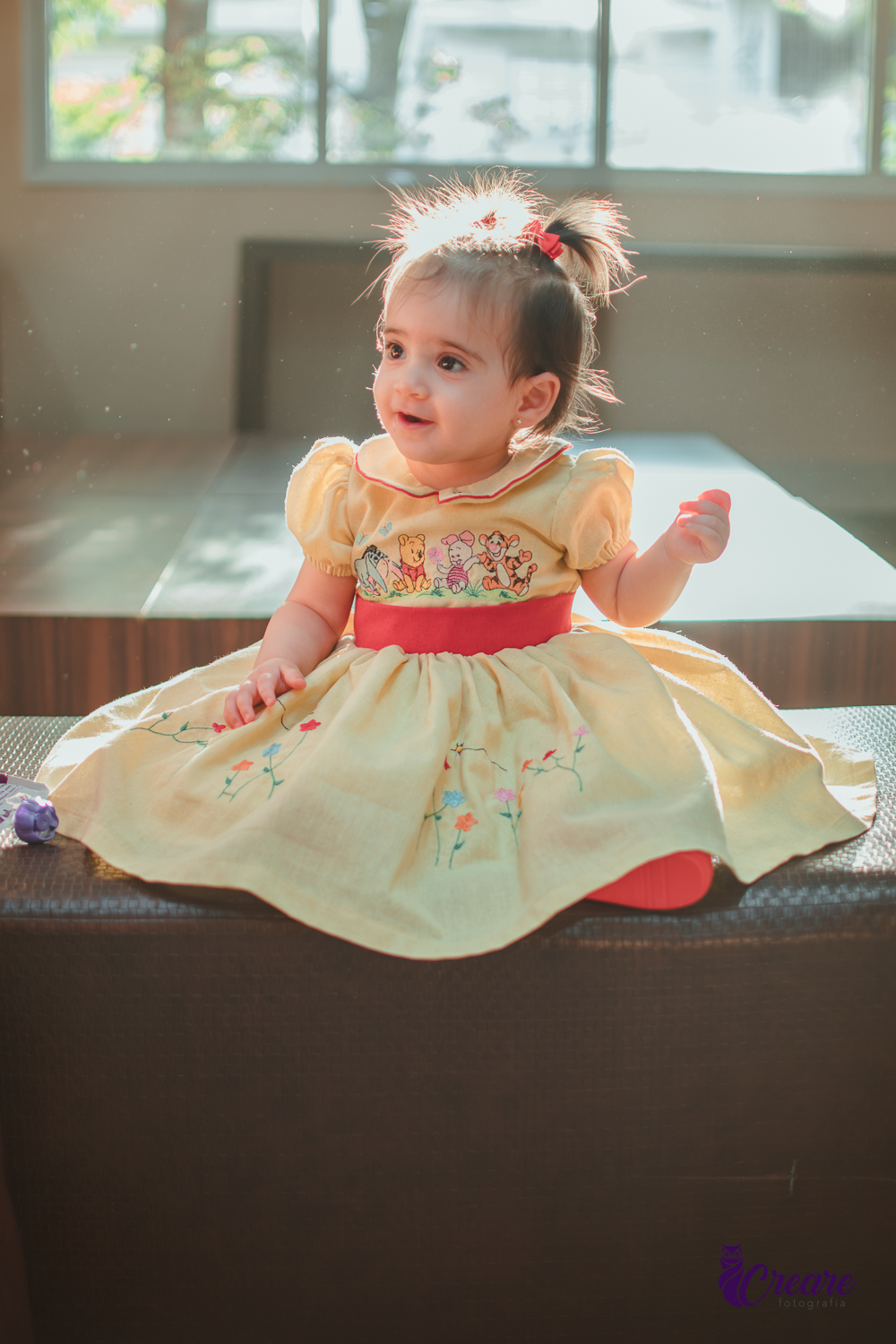 Uma bebê, brincando com reflexos de sol atrás dela, durante sua festa de aniversário de 1 ano feita em casa.