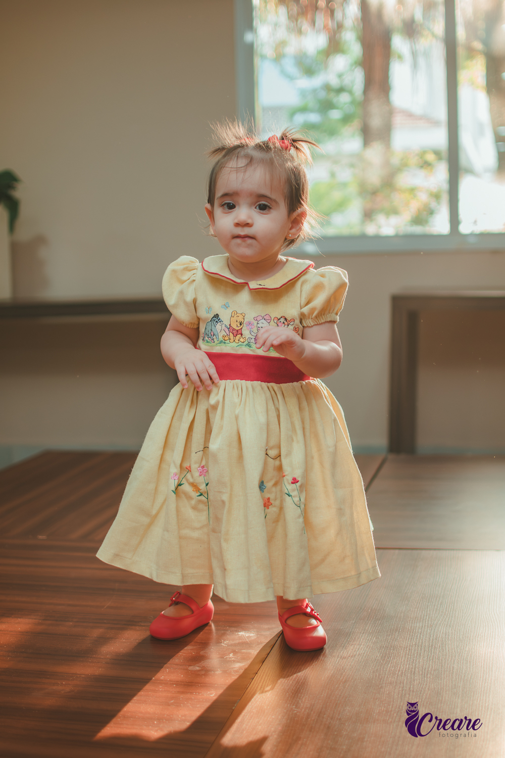 Uma bebê, brincando com reflexos de sol atrás dela, durante sua festa de aniversário de 1 ano feita em casa.