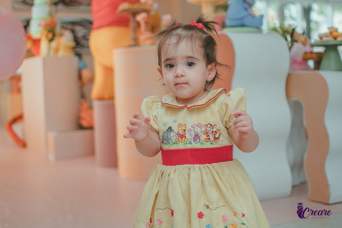 Uma bebê, brincando com reflexos de sol atrás dela, durante sua festa de aniversário de 1 ano feita em casa.
