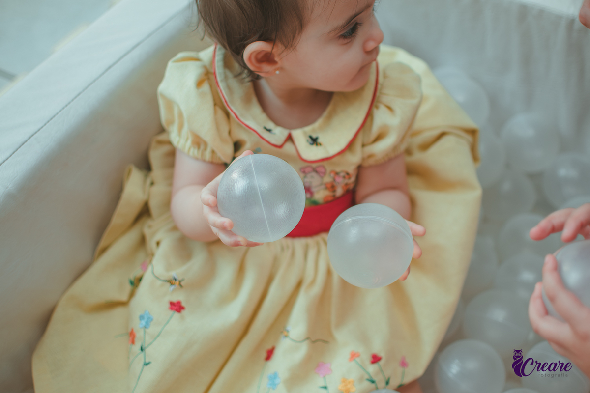 Uma bebê brincando na piscina de bolinhas brancas, durante sua festa de aniversário de 1 ano.