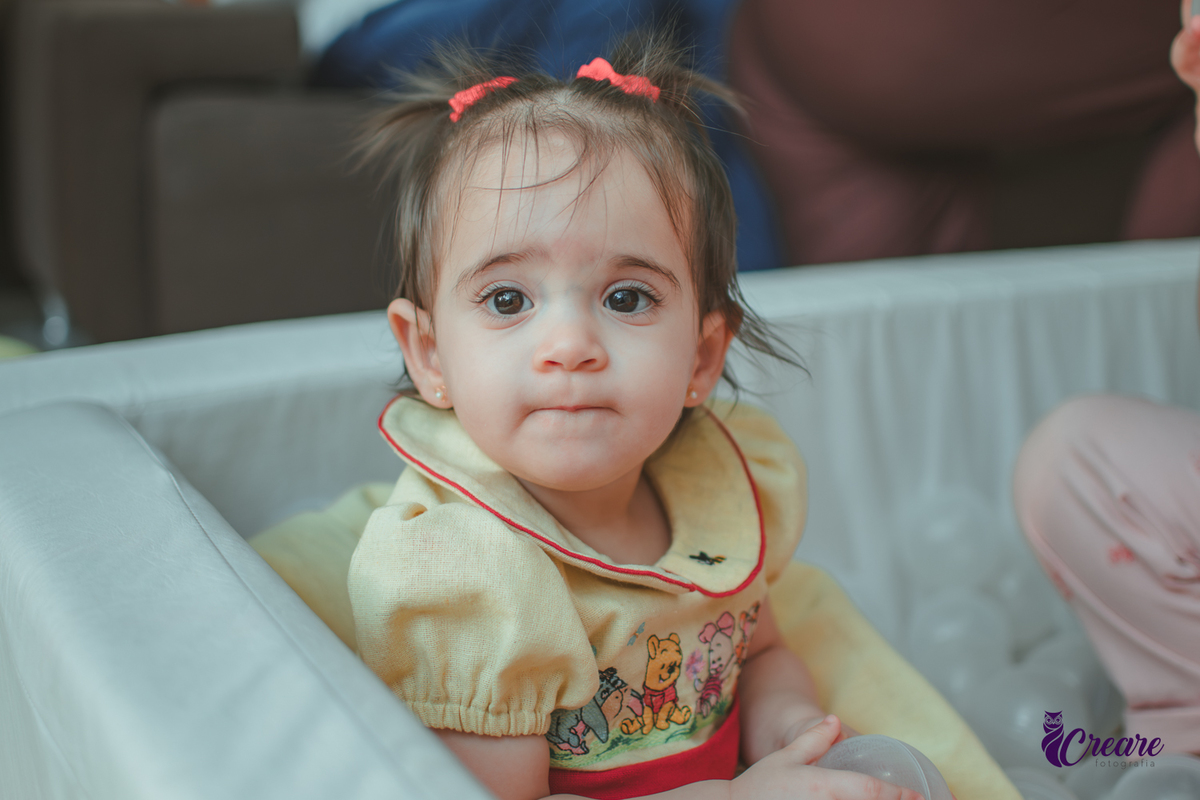Uma bebê brincando na piscina de bolinhas brancas, durante sua festa de aniversário de 1 ano.