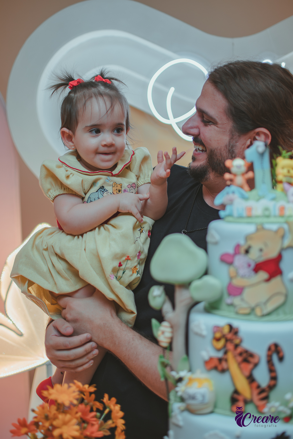 Um homem, em uma decoração de ursinho Pooh, cantando parabéns, durante festa de aniversário de 1 ano.
