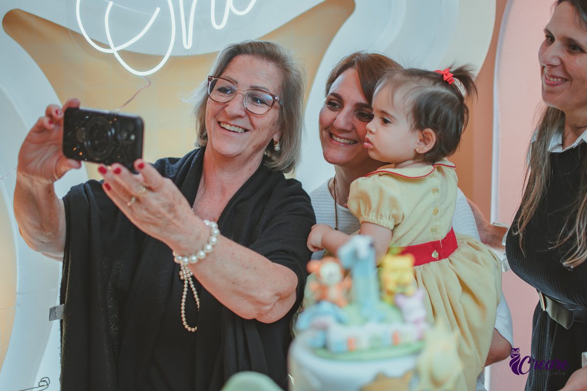 Duas mulheres tirando Selfie com uma bebê de 1 ano, durante festa de anoversário em casa.