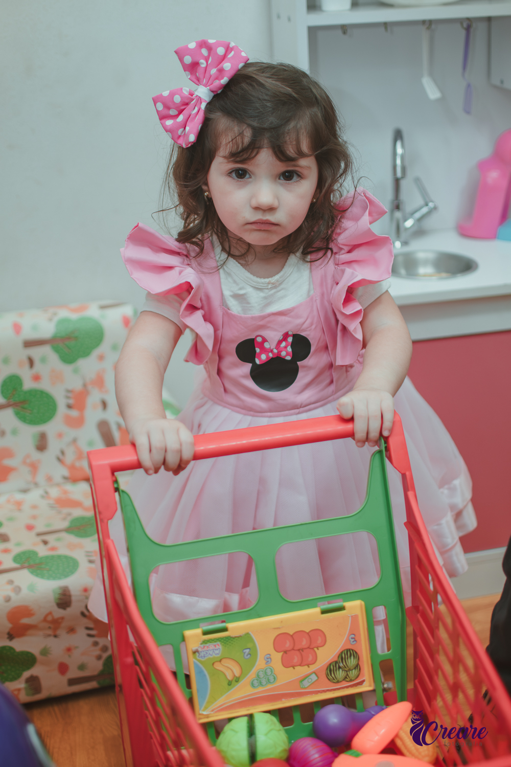 Uma menina brincando na cozinha de madeira, com um carrinho de supermercado de brinquedo, durante sua festa de aniversário de 2 anos em São Caetano do Sul.