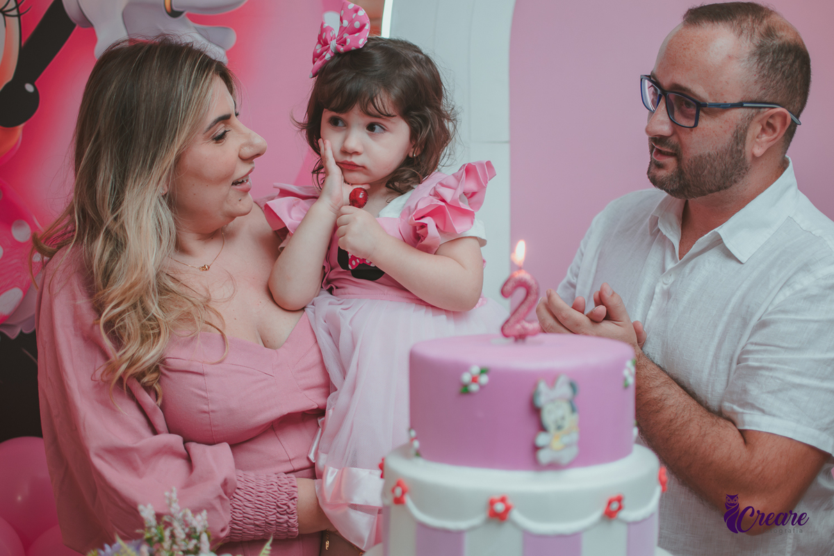 uma familia em frente uma mesa de decoração com tema Minnie, cantando parabéns durante festa de aniversário infantil.