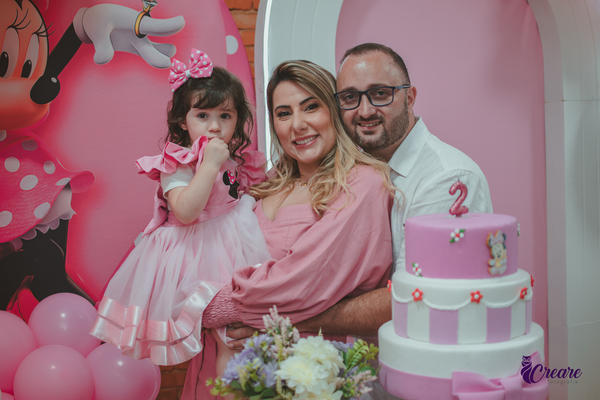 uma familia em frente uma mesa de decoração com tema Minnie,  durante festa de aniversário infantil.