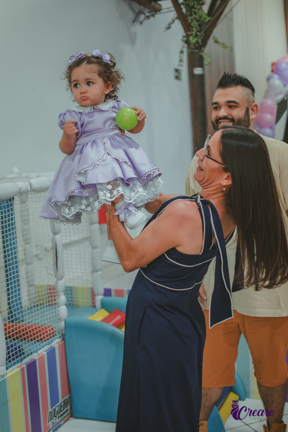 Uma mulher levantando uma Bebê de 1 ano, durante a festa de aniversário infantil.