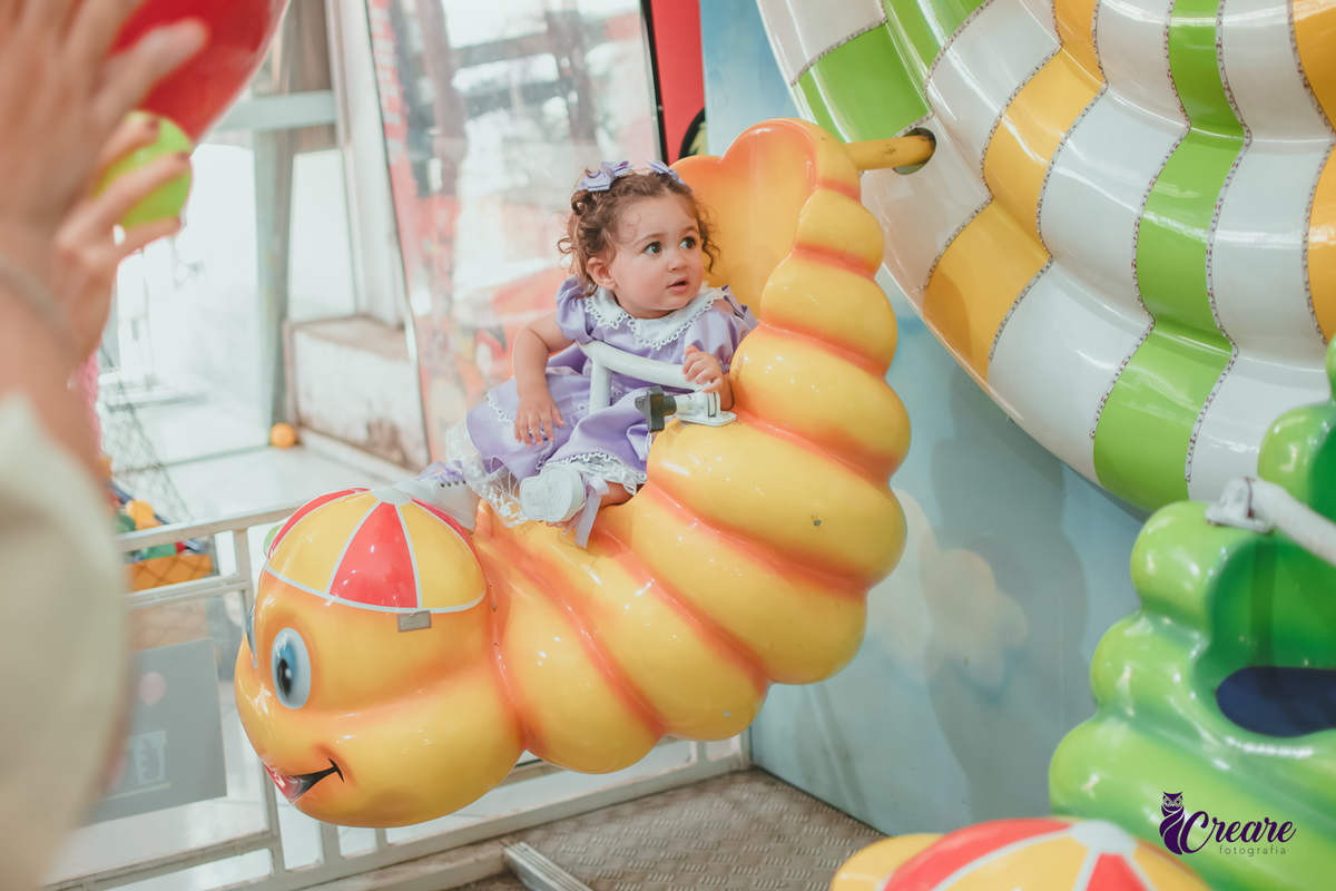 Uma bebê na roda gigante infantil, durante festa de aniversário de 1 ano.