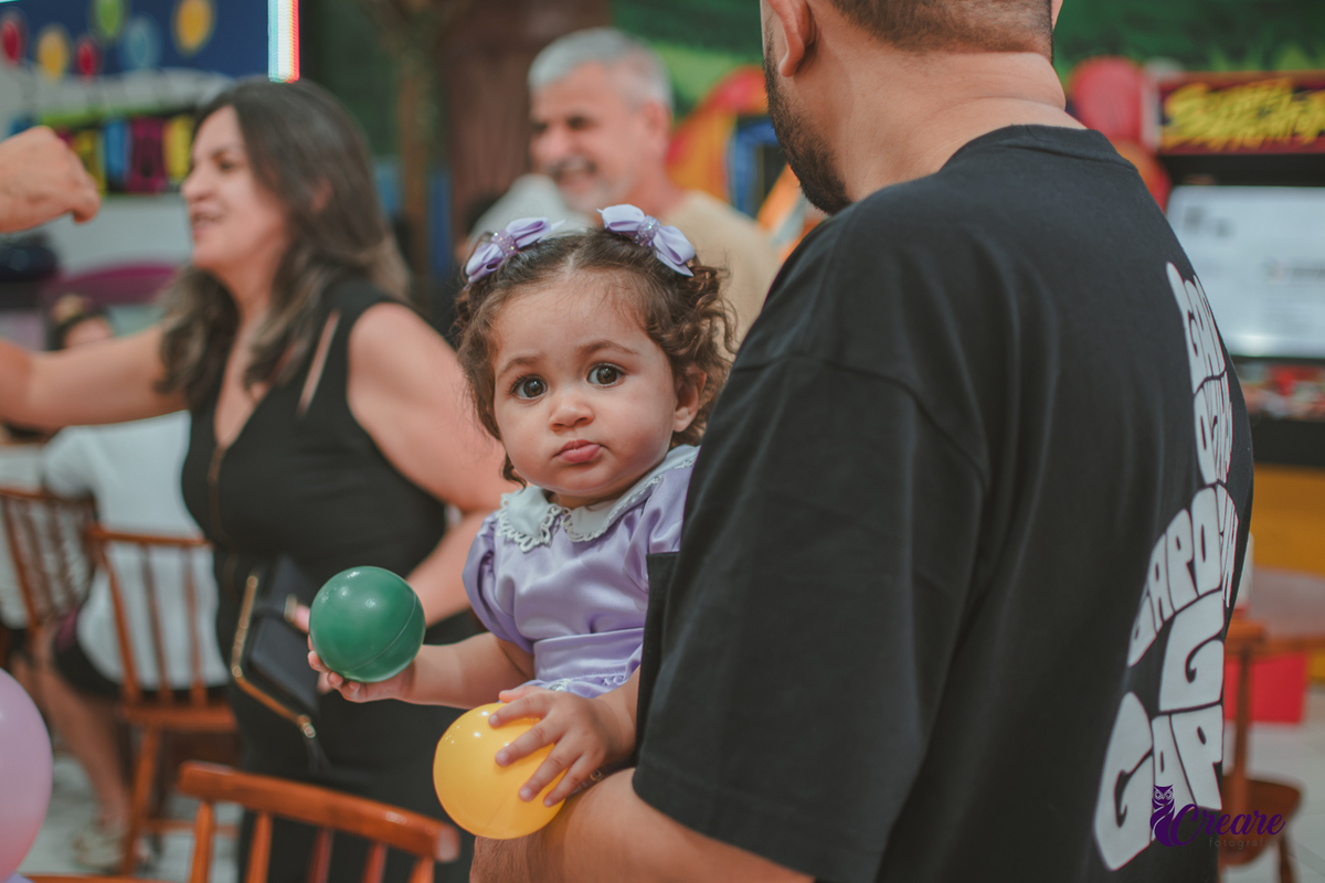 Uma bebê brincando com bolinhas coloridas, durante festa de aniversário de 1 ano.