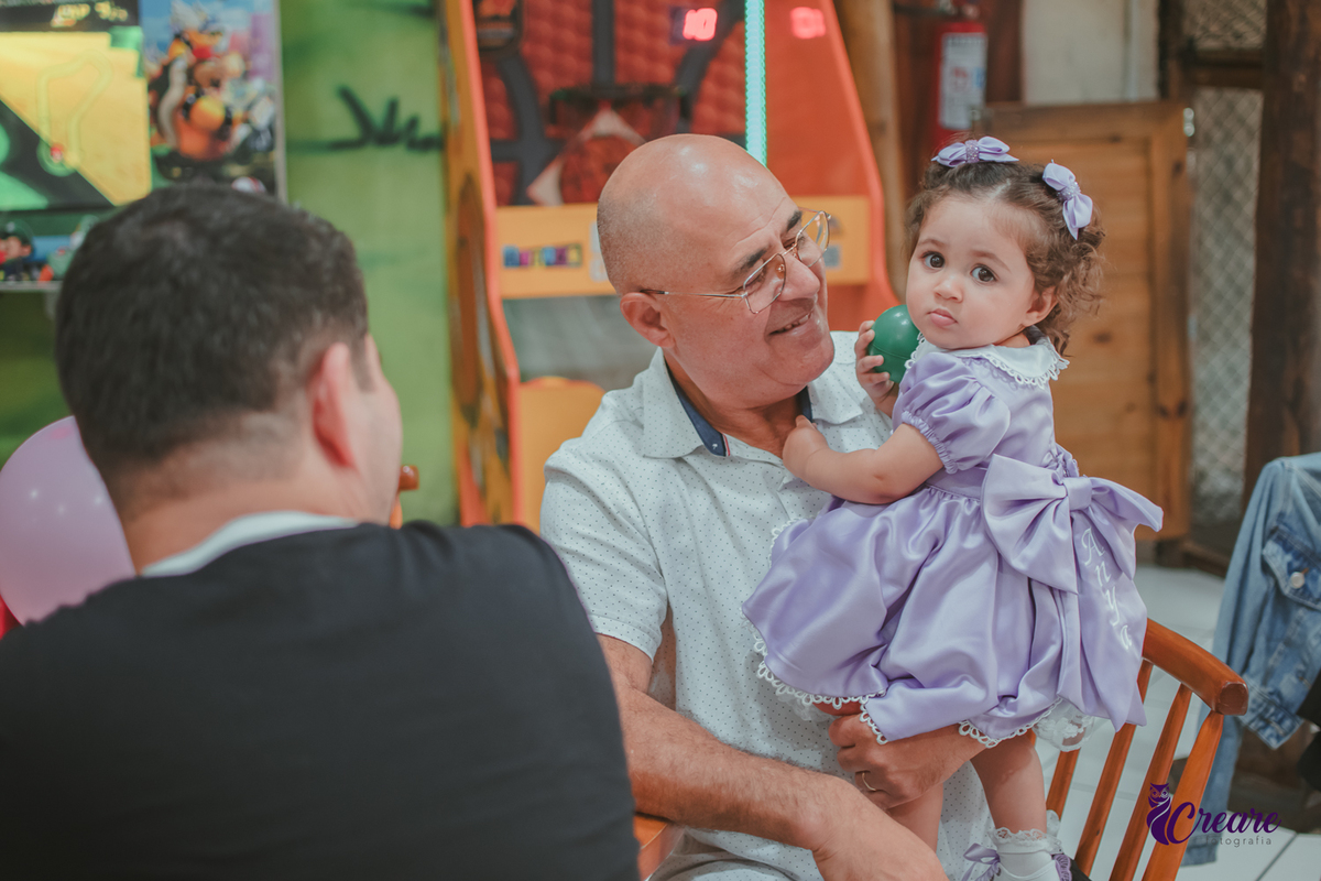 Uma homem de idade, com uma bebê no colo, durante festa de aniversário de 1 ano.