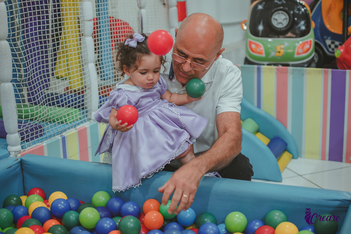 Uma homem de idade, colocando uma bebê na piscina de bolinhas, durante festa de aniversário de 1 ano.