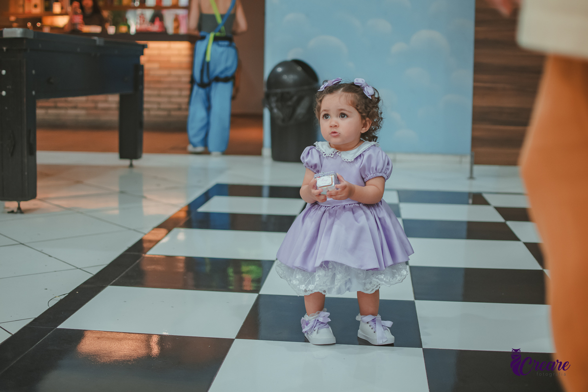 Uma menina usando vestido roxo e andando pelo salão, durante sua festa de aniversário de 1 ano no Buffet É Pique em Mauá.
