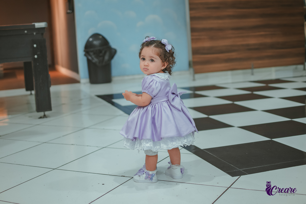 Uma menina usando vestido roxo e andando pelo salão, durante sua festa de aniversário de 1 ano no Buffet É Pique em Mauá.