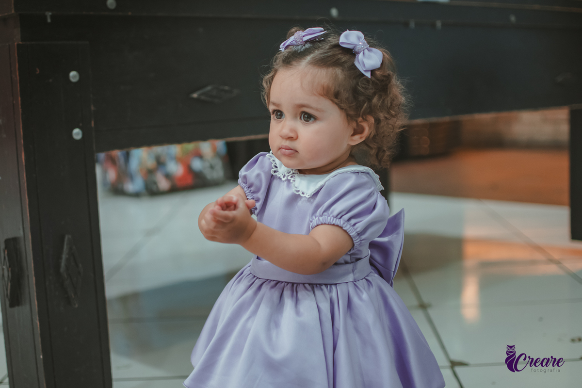 Uma bebê usando vestido roxo e batendo palmas durante seu aniversário de 1 ano.