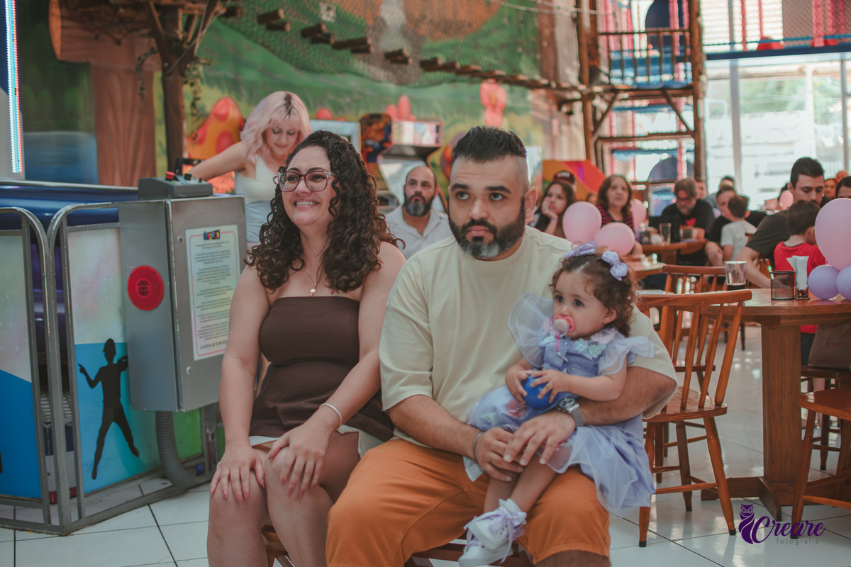 Uma mulher e um homem com bebê no colo, durante retrospectiva em aniversário de 1 ano.